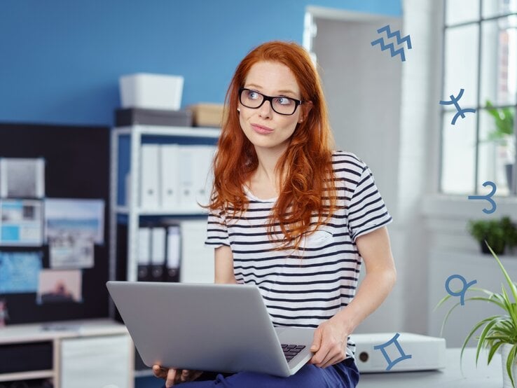 Eine nachdenklich blickende Frau mit rotem Haar und Brille sitzt in einem modernen Büro, während sie einen Laptop hält. Um sie herum sind astrologische Symbole zu sehen, was auf eine astrologische oder horoskopbezogene Arbeits- oder Lebenssituation hinweist.