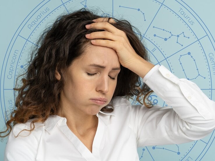 Eine Frau mit lockigem Haar und weißer Bluse hält sich mit geschlossenen Augen die Hand an die Stirn und wirkt erschöpft oder nachdenklich. Im Hintergrund ist ein astrologisches Rad mit den Sternzeichen zu sehen, was auf einen Zusammenhang zwischen ihrem Gemütszustand und astrologischen Einflüssen hinweist.