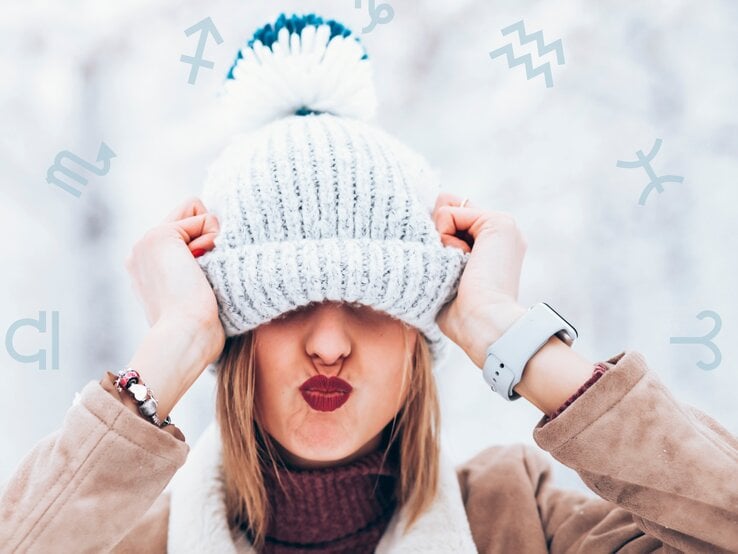 Eine fröhliche Frau in winterlicher Kleidung zieht ihre gestrickte Bommelmütze spielerisch über die Augen und macht einen Kussmund. Der Hintergrund zeigt eine verschneite, helle Szenerie, und astrologische Symbole sind dezent über das Bild verstreut. Das Bild vermittelt Lebensfreude, Verspieltheit und einen Hauch von Astrologie.