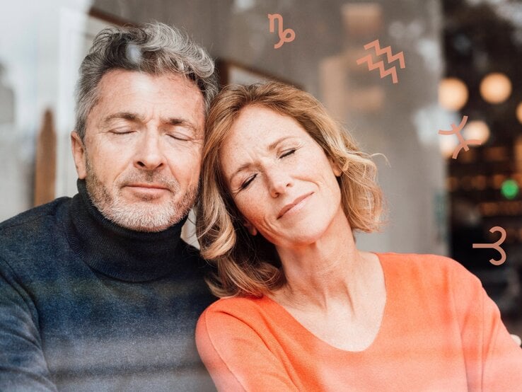 Ein entspanntes Paar mittleren Alters sitzt mit geschlossenen Augen aneinander gelehnt, lächelnd und in harmonischer Stimmung, mit astrologischen Symbolen wie Steinbock und Fische dezent im Bildhintergrund.