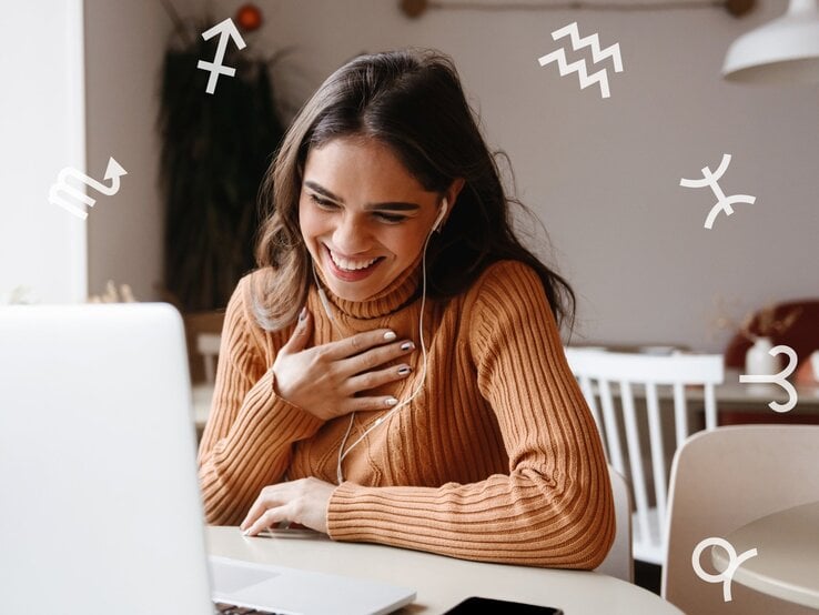 Junge Frau mit langen dunklen Haaren und einem braunen Strickpullover sitzt lächelnd vor einem Laptop. Sie trägt Kopfhörer und hält eine Hand freudig auf ihre Brust. Um sie herum sind weiße astrologische Sternzeichensymbole verteilt.