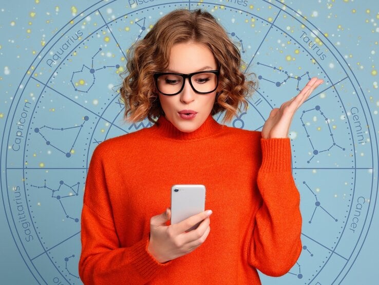  Eine junge Frau mit blonden, lockigen Haaren und einer schwarzen Brille hält ein Smartphone in der Hand und schaut überrascht oder nachdenklich darauf. Sie trägt einen leuchtend orangefarbenen Pullover. Im Hintergrund ist ein astrologisches Rad mit den Sternzeichen und funkelnden goldenen Details auf einem hellblauen Hintergrund zu sehen. Das Bild kombiniert moderne Technologie mit einem Hauch von Mystik und Astrologie und vermittelt eine dynamische, nachdenkliche Atmosphäre.