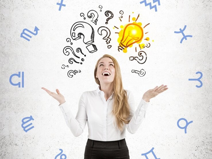 Eine junge Frau mit langen blonden Haaren trägt eine weiße Bluse und schaut lächelnd nach oben. Über ihrem Kopf sind gezeichnete Fragezeichen und eine leuchtende Glühbirne als Symbol für eine plötzliche Eingebung oder Idee. Im Hintergrund schweben astrologische Sternzeichen in blauer Farbe auf einer strukturierten, weißen Wand. Die Szene vermittelt Kreativität, Inspiration und die Verbindung zwischen Intuition und Astrologie.