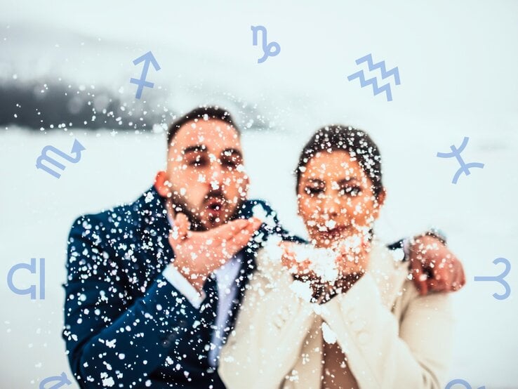 Ein fröhliches Paar in eleganter Winterkleidung steht in einer verschneiten Landschaft. Beide halten Schnee in ihren Händen und pusten ihn spielerisch in die Luft, wodurch Schneeflocken um sie herumwirbeln. Der Mann trägt einen dunkelblauen Anzug, die Frau einen cremefarbenen Mantel. Ihr Gesichtsausdruck strahlt Freude und Romantik aus. Im Hintergrund sind schneebedeckte Hügel und eine winterliche Landschaft zu erkennen. Um das Paar herum schweben verschiedene astrologische Symbole, darunter für Schütze, Skorpion, Wassermann und Fische, was eine Verbindung zur Astrologie und zu einem Flirthoroskop suggeriert.