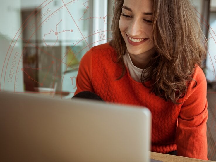 Eine lächelnde Frau mit schulterlangem braunen Haar sitzt an einem Tisch und schaut auf ihren Laptop-Bildschirm. Sie trägt einen roten Pullover. Im Hintergrund ist eine dezente, transparente Grafik eines Horoskop-Kreises mit Sternzeichen und Konstellationen eingeblendet.