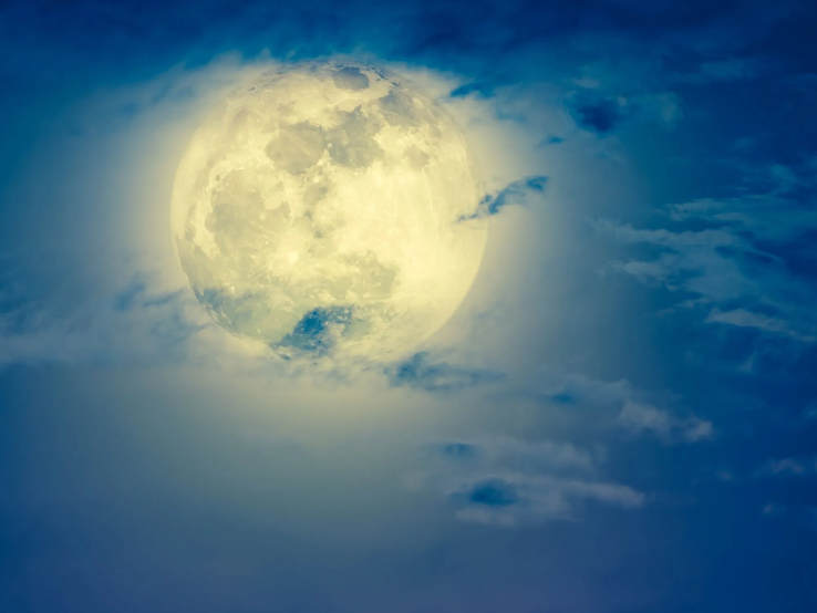 Mondhoroskop Oktober 2025: Heller Vollmond am Nachthimmel, umgeben von leicht ziehenden Wolken in Blau- und Weißtönen.