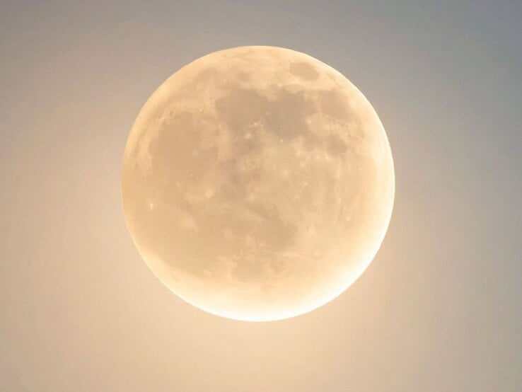 Ein Vollmond am Nachthimmel mit sanftem, goldenem Schimmer. Die Oberflächenstrukturen des Mondes, wie Krater und Ebenen, sind klar erkennbar. Der Himmel wirkt leicht aufgehellt und hat nur einen dezenten Blauton.