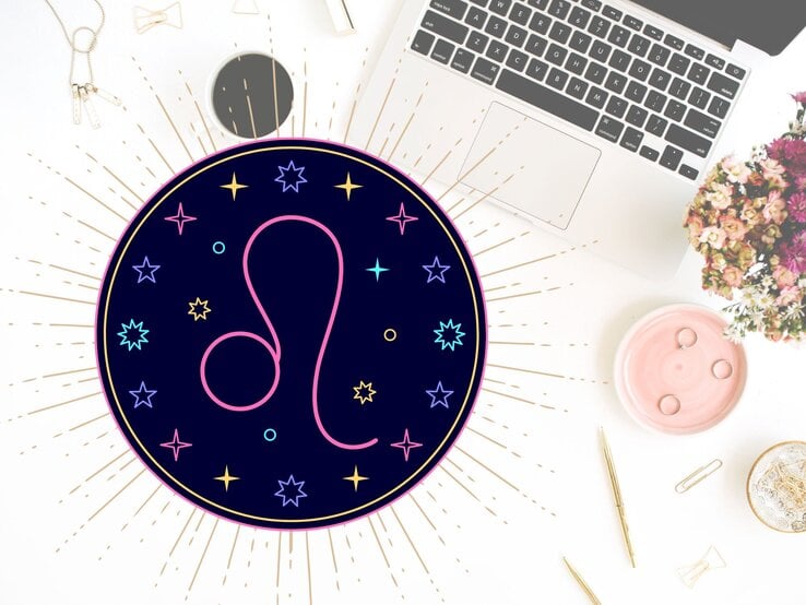 Draufblick auf einen Schreibtisch mit verschiedenen Utensilien wie goldene Kugelschreiber, Sicherheitsnadeln und der Tastatur eines Laptops. Links daneben das grafische Symbol des Sternzeichens Löwe in einem dunkelblauen Kreis umgeben von gelben, pinken und hellblauen Sternen. | © Floral Deco, Julia Dreams und warmjuly via Canva.com [M]