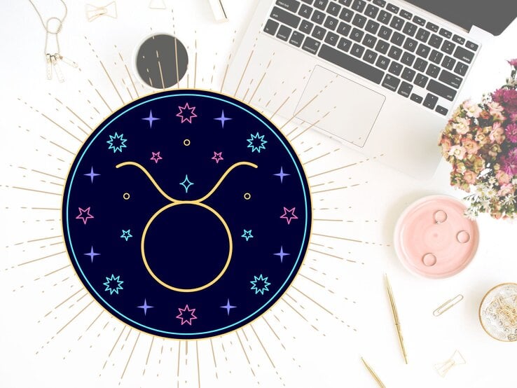 Draufblick auf einen Schreibtisch mit verschiedenen Utensilien wie goldene Kugelschreiber, Sicherheitsnadeln und der Tastatur eines Laptops. Links daneben das grafische Symbol des Sternzeichens Stier in einem dunkelblauen Kreis umgeben von gelben, pinken und hellblauen Sternen. | © Floral Deco, Julia Dreams und warmjuly via Canva.com [M]