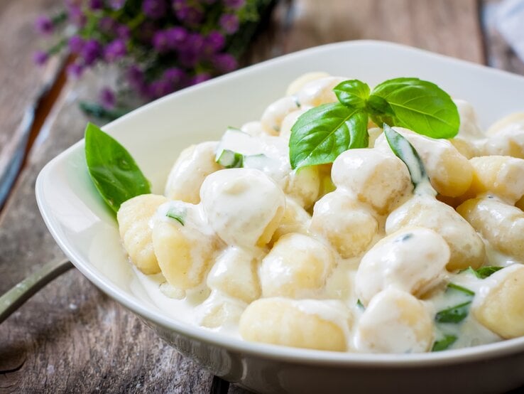 Ein weißer Teller befüllt mit Low-Carb-Gnocchi in cremiger Soße auf Holztisch. | © AdobeStock/Ramon Grosso
