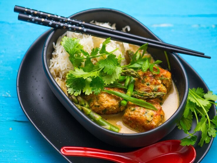 Eine dunkle schale mit der Suppe und Reis auf blauem Untergrund.