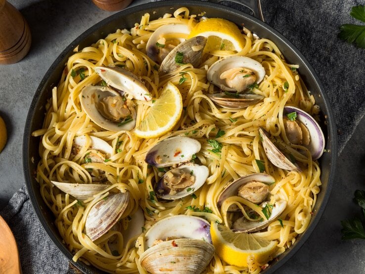 Ein schwarzer Teller mit einer Portion Spaghetti Vongole auf einem grauen Tisch von oben fotografiert