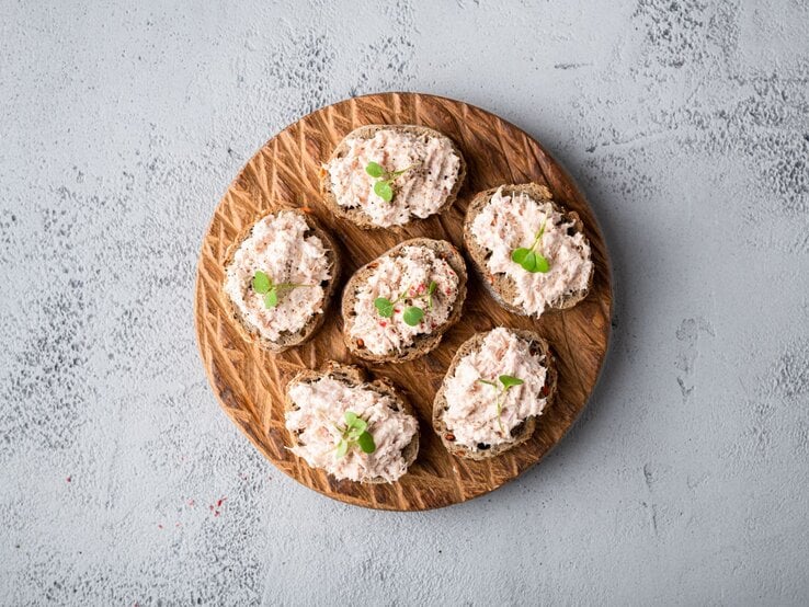 Draufsicht auf  ein Holzbrett, darauf mehrere Scheiben Thunfisch-Bruschetta.