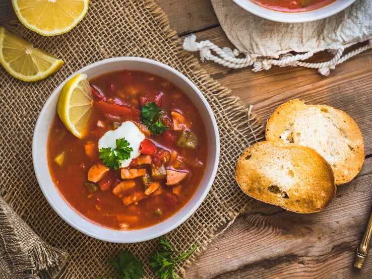 Draufsicht auf eine braune Schale gefüllt mit Soljanka. Das Ganze steht auf einem Holztisch. 