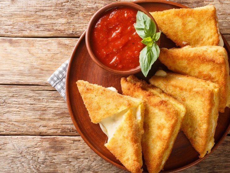 Das Sandwich auf einem braunen Teller und Holztisch mit einem Schälchen Tomatensoße serviert. Alles direkt von oben fotografiert.