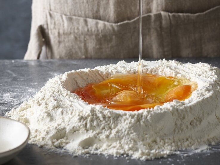 Angehäuftes Mehl mit Mulde auf Arbeitsfläche / rohes Ei in Mulde / Frontalsicht