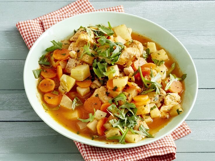 Ein heller Teller mit dem Ragout auf einem hellen Holztisch mit rot-weiß-karierter Tischdecke