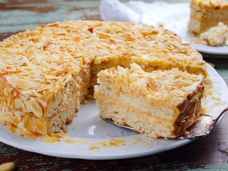 Die Torte auf einem rustikalen Holztisch mit Mandelblättchen drum herum. Alles direkt von vorne fotografiert. | © Shutterstock/ hlphoto