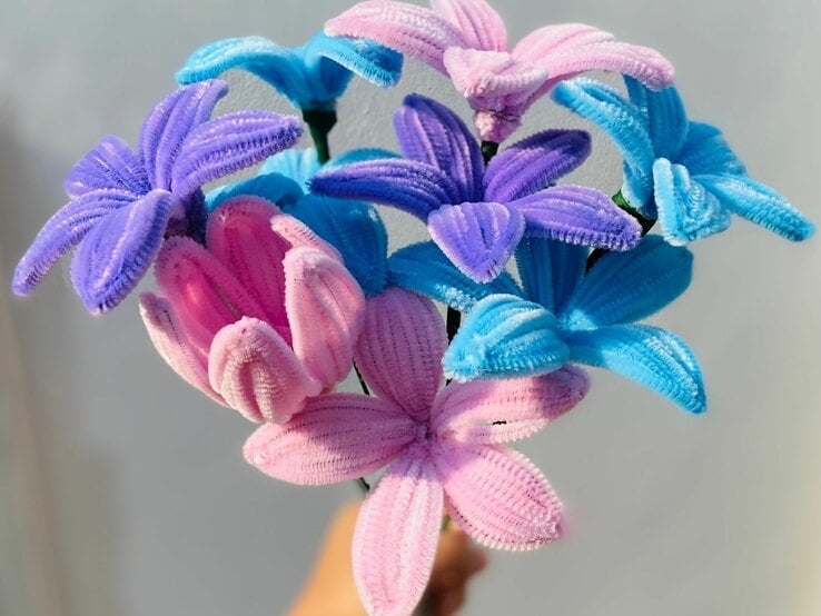Ein bunter Strauß aus Pfeifenputzer-Blumen in Blau-, Lila- und Rosatönen vor grauem Hintergrund. | © Shutterstock/Galeryintan