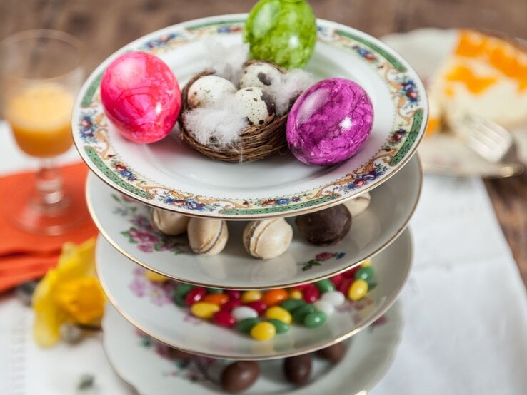 Eine elegante Etagere aus verzierten Porzellantellern mit Ostereiern, Pralinen, Macarons und bunten Süßigkeiten.