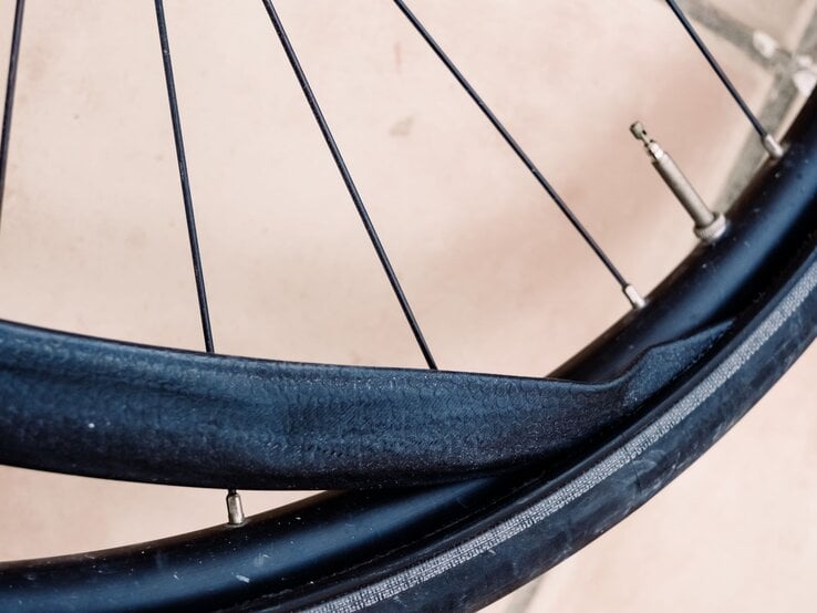Nahaufnahme eines Fahrradreifens mit stark beschädigtem, aufgerissenem Fahrradschlauch vor hellem Untergrund.
