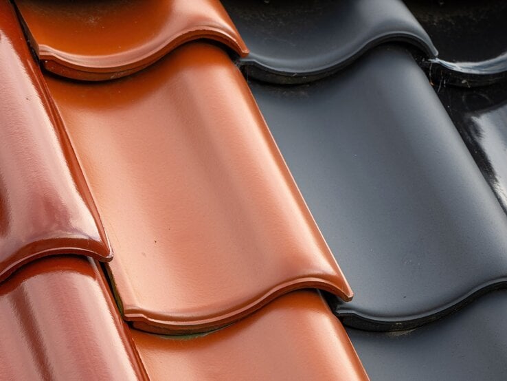 Glänzende Dachziegel in Ziegelrot und Anthrazit liegen dicht nebeneinander in leicht geschwungener Form.