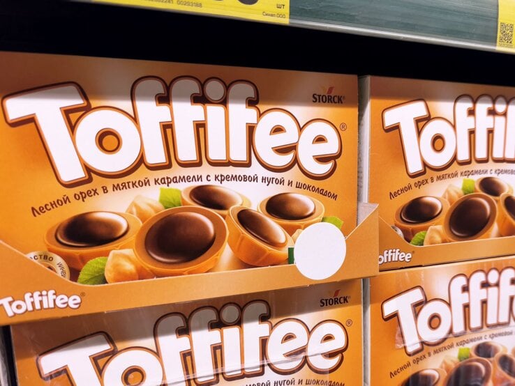 Nahaufnahme eines Supermarktregals mit orangefarbenen Toffifee-Schachteln und Preisschildern in kyrillischer Schrift.