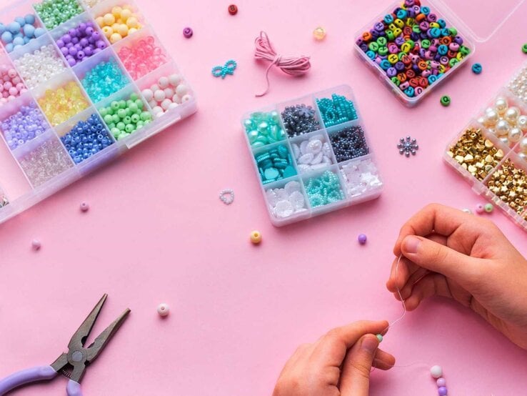 Erstellen von buntem Perlenschmuck mit verschiedenen Perlen und Bastelwerkzeugen auf einer hellrosa Oberfläche