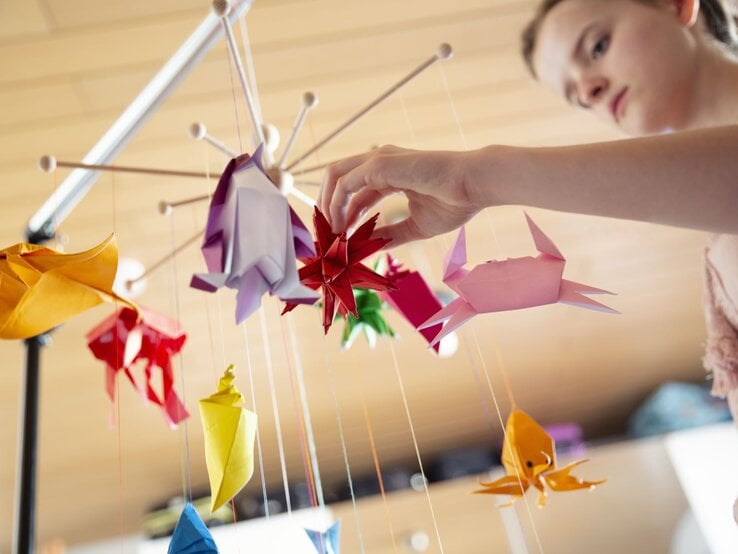 Teenager-Mädchen bastelt ein Mobile fürs Babybett mit selbstgemachten bunten Origami-Skulpturen
