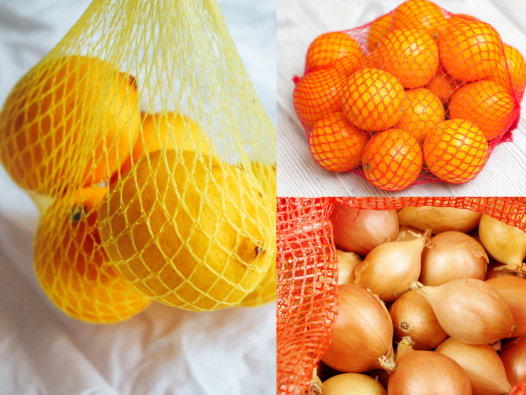 Drei Netze mit Zitrusfrüchten und Zwiebeln liegen auf weißem Untergrund: Zitronen, Mandarinen und goldgelbe Zwiebeln.