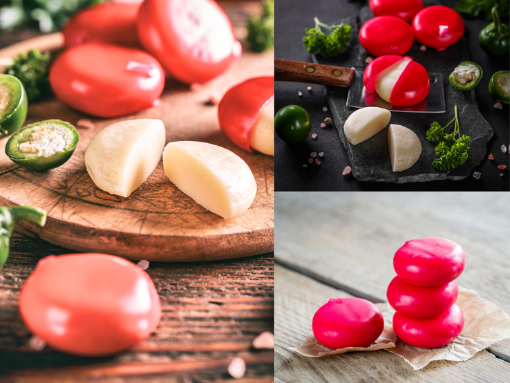Runde Mini-Käselaibe mit rotem Wachs, teils aufgeschnitten, liegen gestapelt oder auf Brettern mit Kräutern, Chili und Salz.