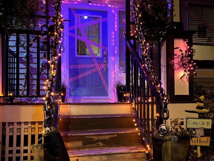 Hauseingang gestalten für Halloween: Mit Lichterketten, Ketten, Skeletten und Spinnennetzen gruselig geschmückter Hauseingang bei Nacht.