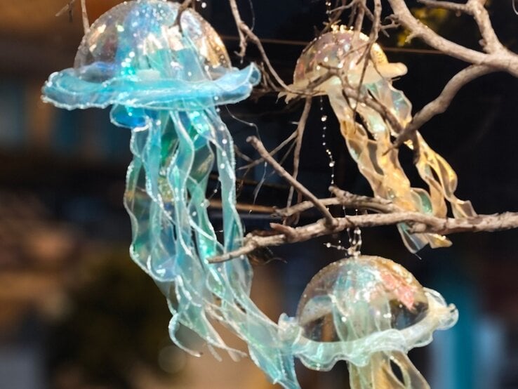 Drei schimmernde Quallenlaternen aus transparentem Stoff hängen leuchtend zwischen kahlen Ästen im Dunkel der Nacht.