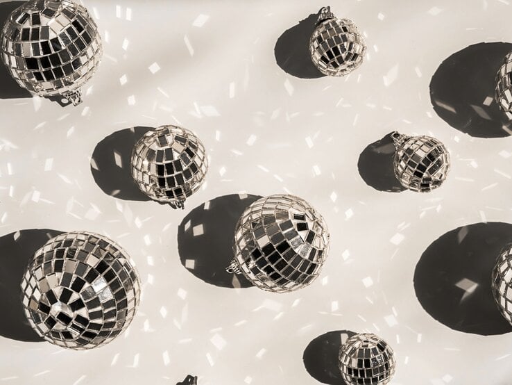 Mehrere glänzende Discokugeln werfen tanzende Lichtreflexe und runde Schatten auf einen hellen Untergrund.