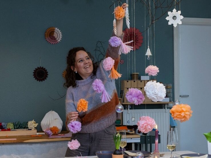 Papierkünstlerin Eva Maria Berg dekoriert mit selbstgemachten Papierblumen einen Zweig.