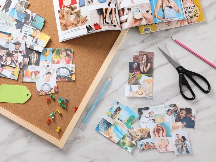 Auf einem Schreibtisch liegen ausgeschnittene Fotos, bunte Reißzwecken, Scheren und Zeitschriften für ein Vision Board.