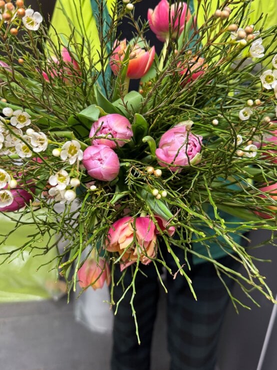 Frischer Strauß aus rosafarbenen Tulpen und weißen Wachsblumen, kunstvoll gebunden mit viel Grün im Hintergrund. | © Madeleine Liedke 