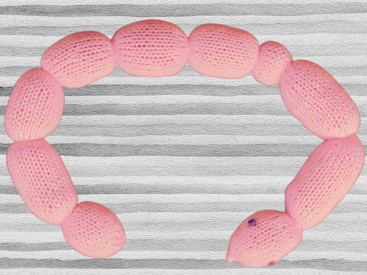 Rosa gestricktes Spielzeug in Form einer gedrehten Schlange auf gestreiftem grauen Hintergrund liegend. | © Canva / AI [M]