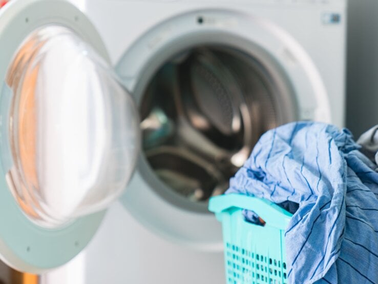 Geöffnete Waschmaschine mit frischer Wäsche neben voller blauer Wäschekorb.