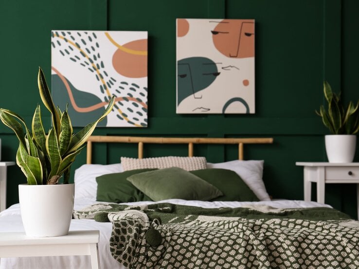 Modern eingerichtetes Schlafzimmer mit grünem Wandanstrich, Pflanzen in weißen Töpfen und abstrakter Kunst über dem Bett.