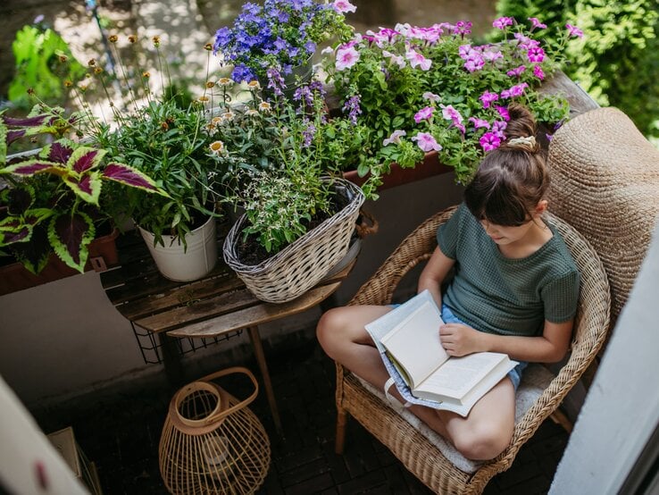 Zu sehen ist eine Frau, die auf ihrem Balkon entspannt, der voller Pflanzen ist.