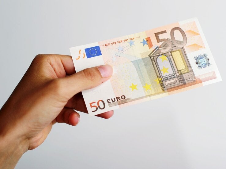 Ein 50-Euro-Schein wird von einer Hand mit leicht gebogenen Fingern gehalten, vor einem schlichten weißen Hintergrund.