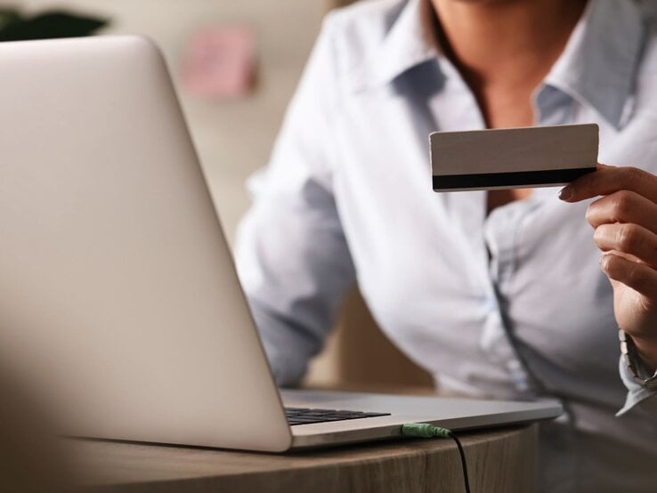 Zu sehen ist eine Frau, die eine Kreditkarte hält und am Laptop sitzt.