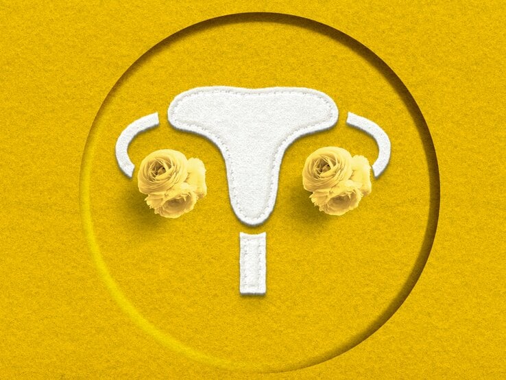 Gestickte Gebärmutter auf gelbem Filzhintergrund mit gelben Ranunkelblüten an den Eierstöcken als künstlerische Darstellung.