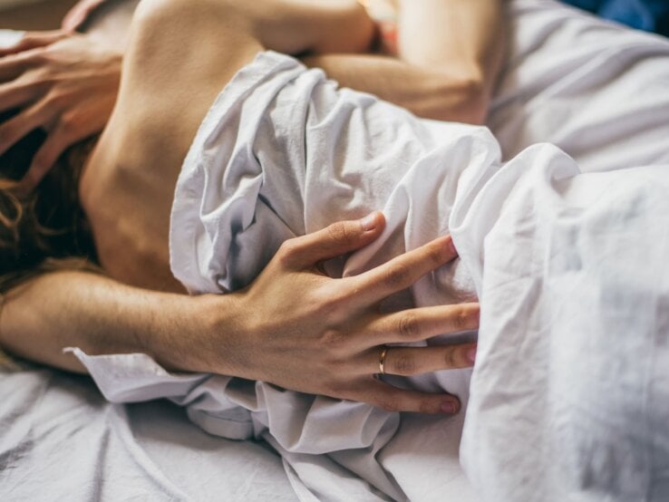 Intime Szene zweier Personen, die sich unter einer Bettdecke eng umschlingen.