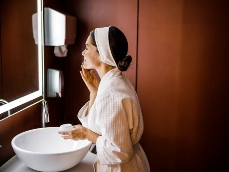 Frau führt vor Spiegel Beauty-Routine am Abend durch