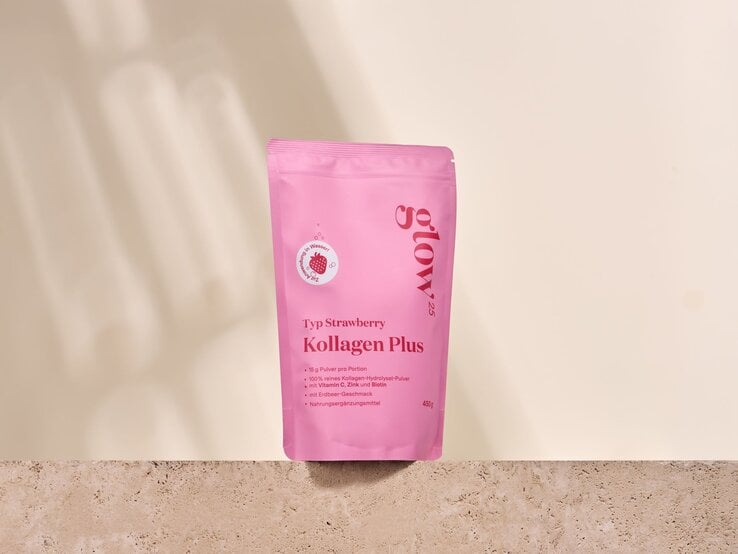 Pinke Verpackung „Kollagen Plus Typ Strawberry“ steht auf beigem Stein vor hellcremer Wand mit weichen Schatten. | © Glow25