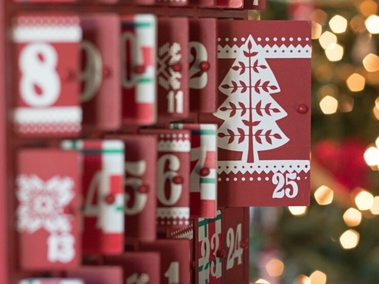 Roter Adventskalender mit weißen Zahlen und Weihnachtsbaum-Motiv auf Tür 25, weitere Türen teilweise geöffnet.