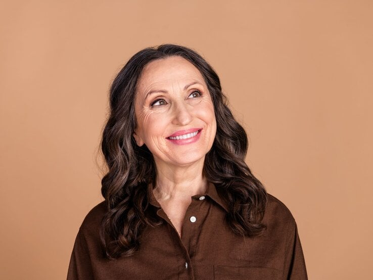 Attraktive Frau mit braunen, leichten Locken, die seitlich nach oben guckt.