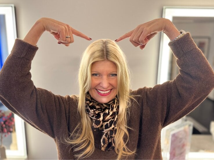 Renate Zott nach dem Haare färben deutet mit beiden Zeigefingern auf ihren frisch gefärbten Haaransatz im Friseursalon. | © Renate Zott